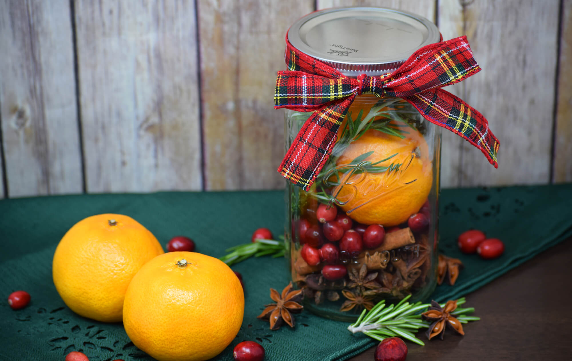 A mason jar filled with Christmas smells, such as mulling spices and cranberries, on a green tablecloth