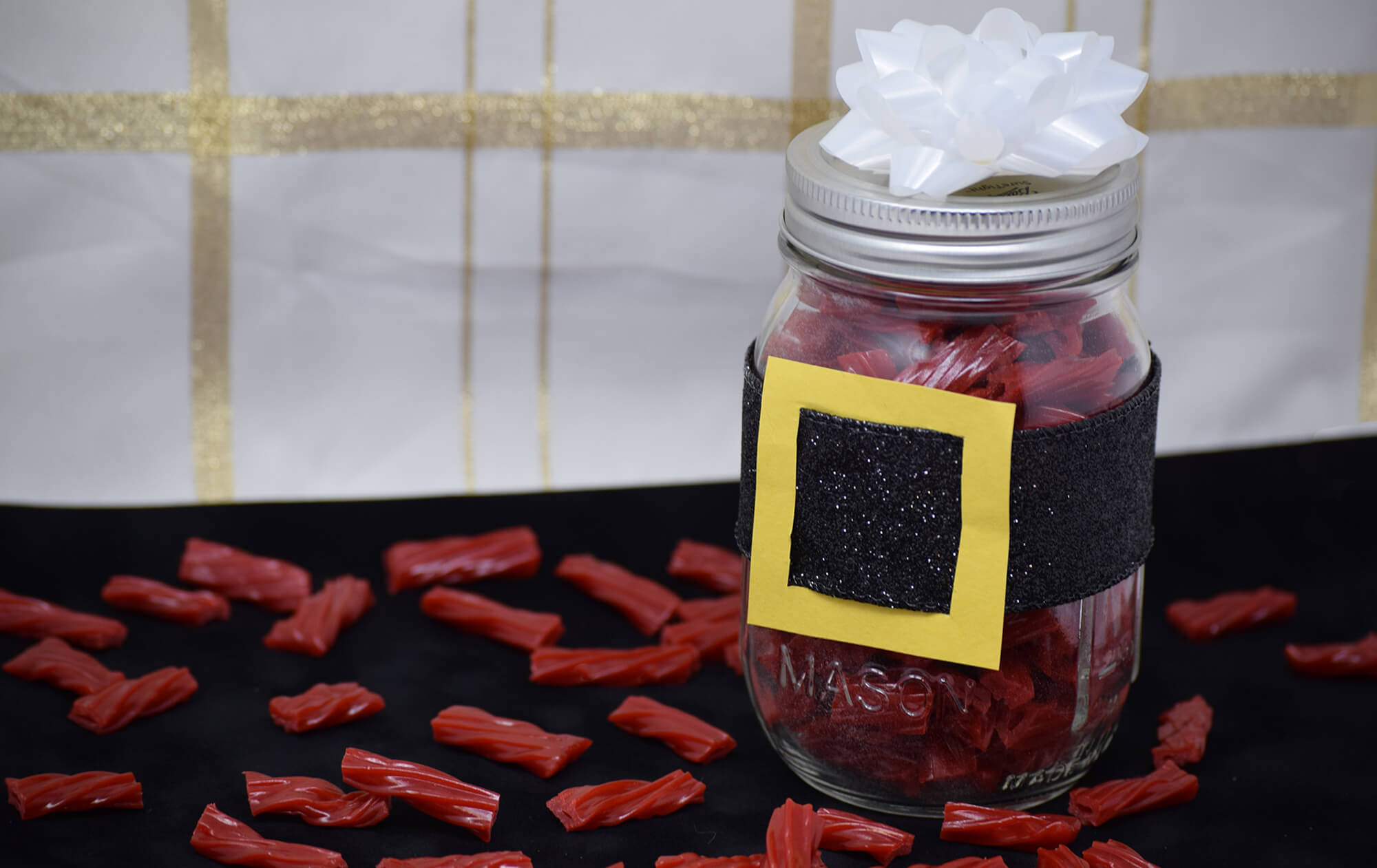 A mason jar filled with licorice with a Santa belt around it