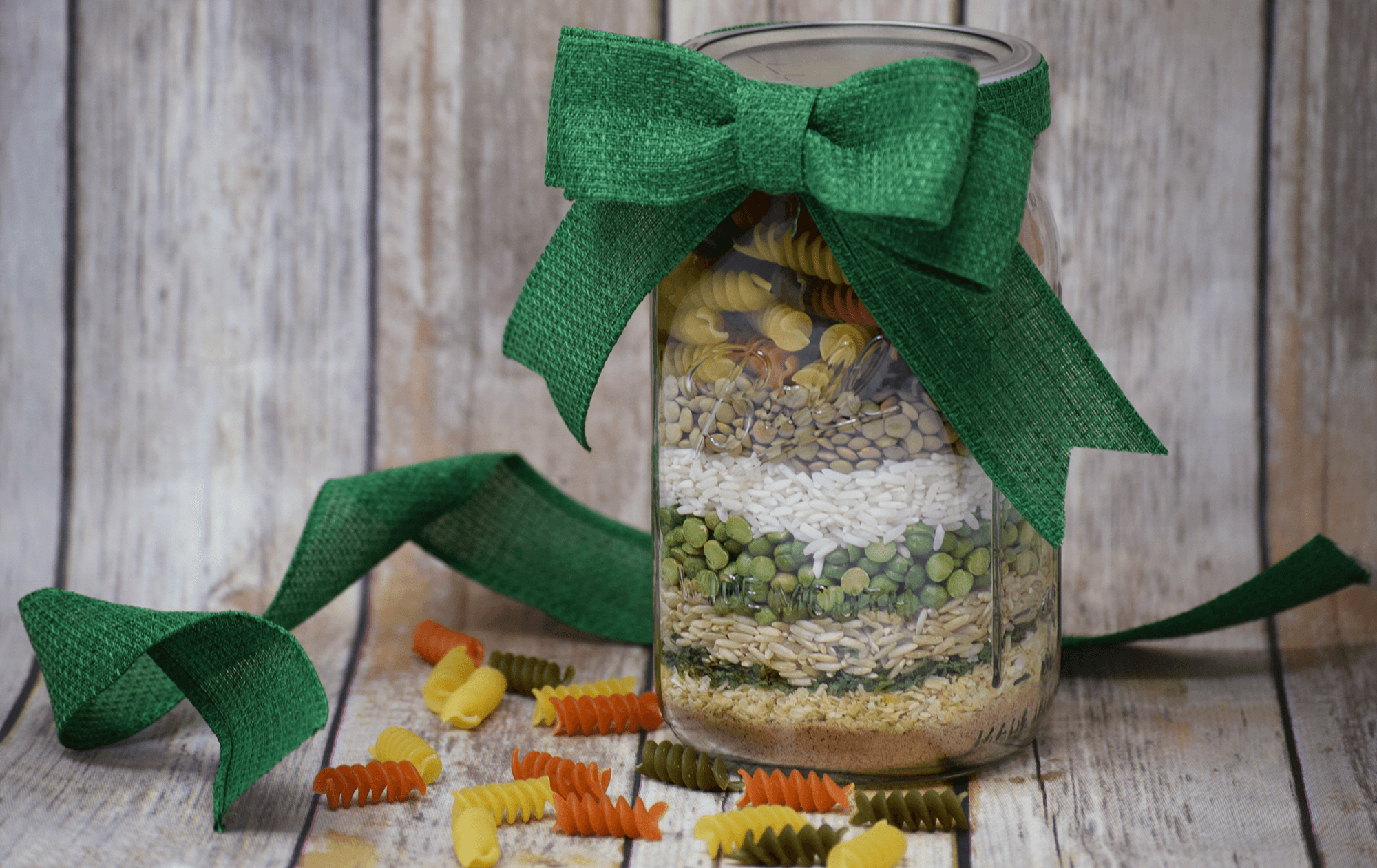 A mason jar with soup ingredients, such as pasta, lentils, split peas and rice, inside of it